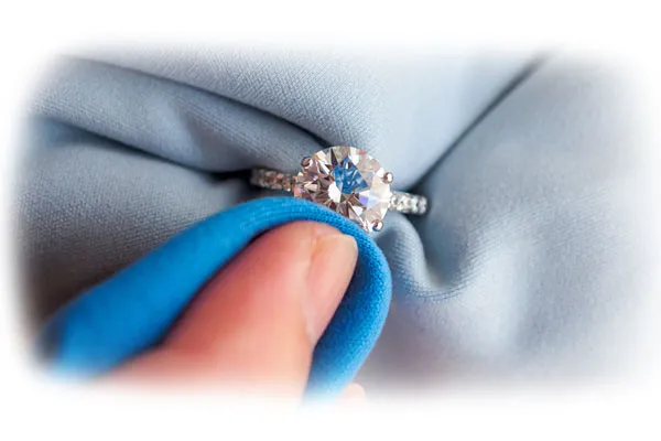 Close-up of a ring being cleaned with a blue cloth, emphasizing the importance of jewelry care