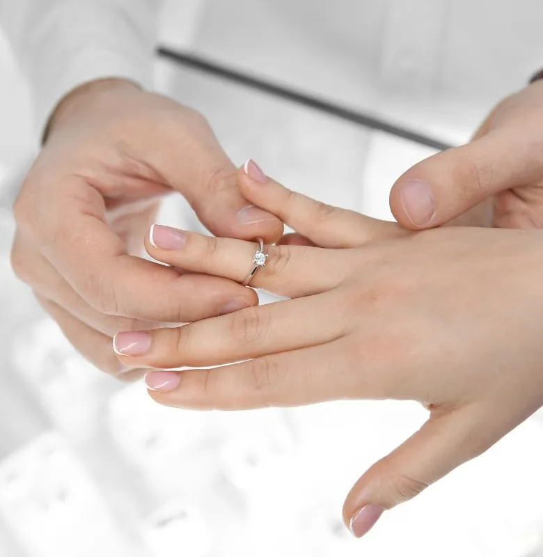 Man placing diamond engagement ring on woman's finger in store